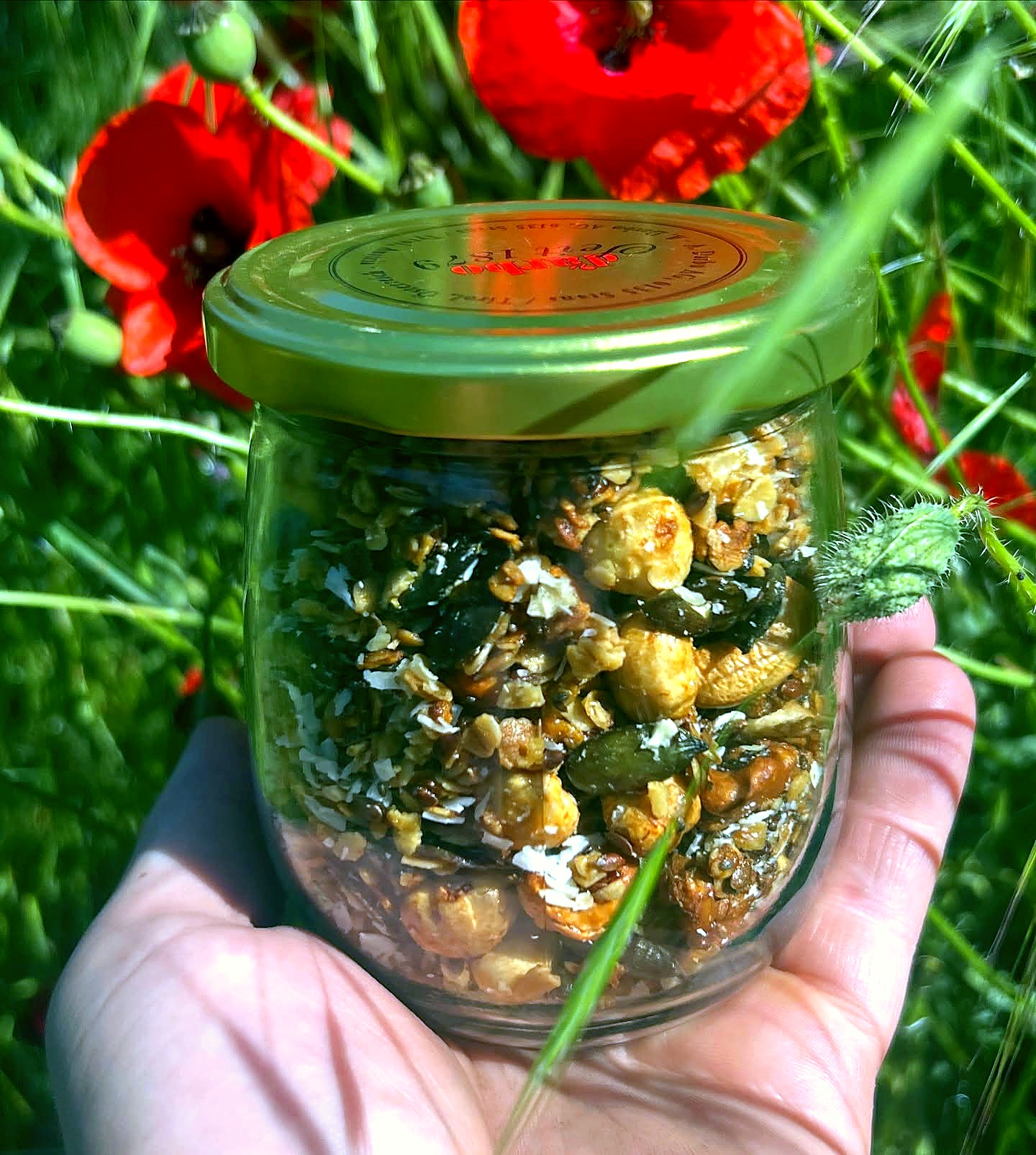 Hand hält Einweckglas mit hausgemachtem Granola vor Mohnblumen – Hausgemachtes von Fritzi