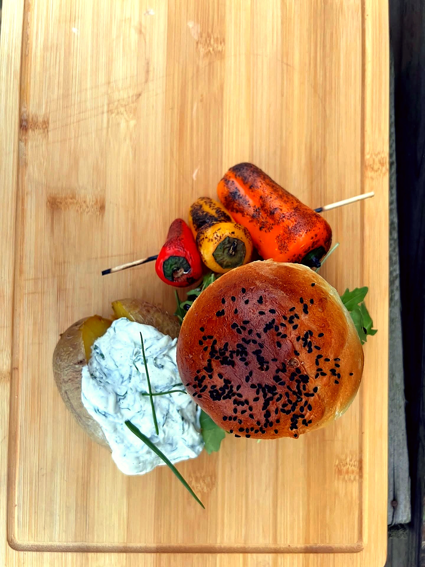 Rustikales Holzbrett mit Sesam-Brioche, Ofenkartoffel mit Kräuterquark und gegrillter Paprika – Catering im Grünen